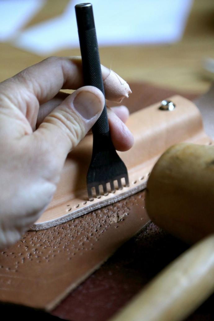 Artisan cousant du cuir à la main avec une aiguille et du fil ciré, technique traditionnelle pour une finition robuste.